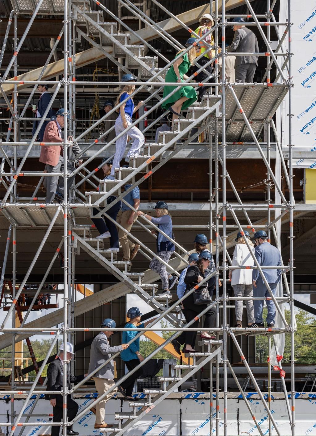 A group of people in construction hats climb the stairs of a building under construction